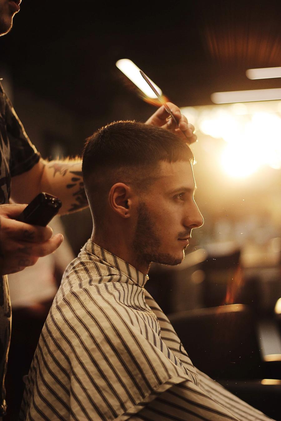 A barber shaping a men’s haircut with clippers and a comb