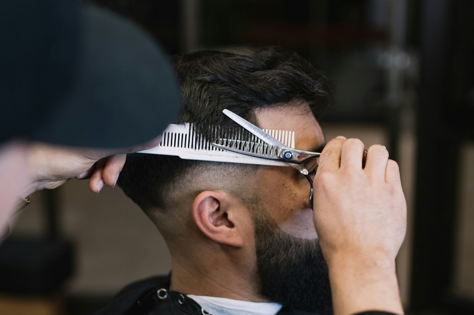 A barber cutting a client’s hair with scissors and a comb